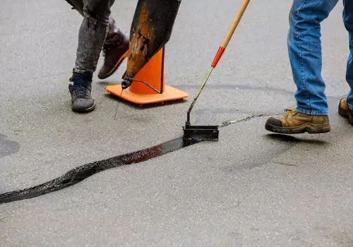 Two men repairing a crack in the road with asphalt binder mixture for an asphalt repair in Bloomington IL. 